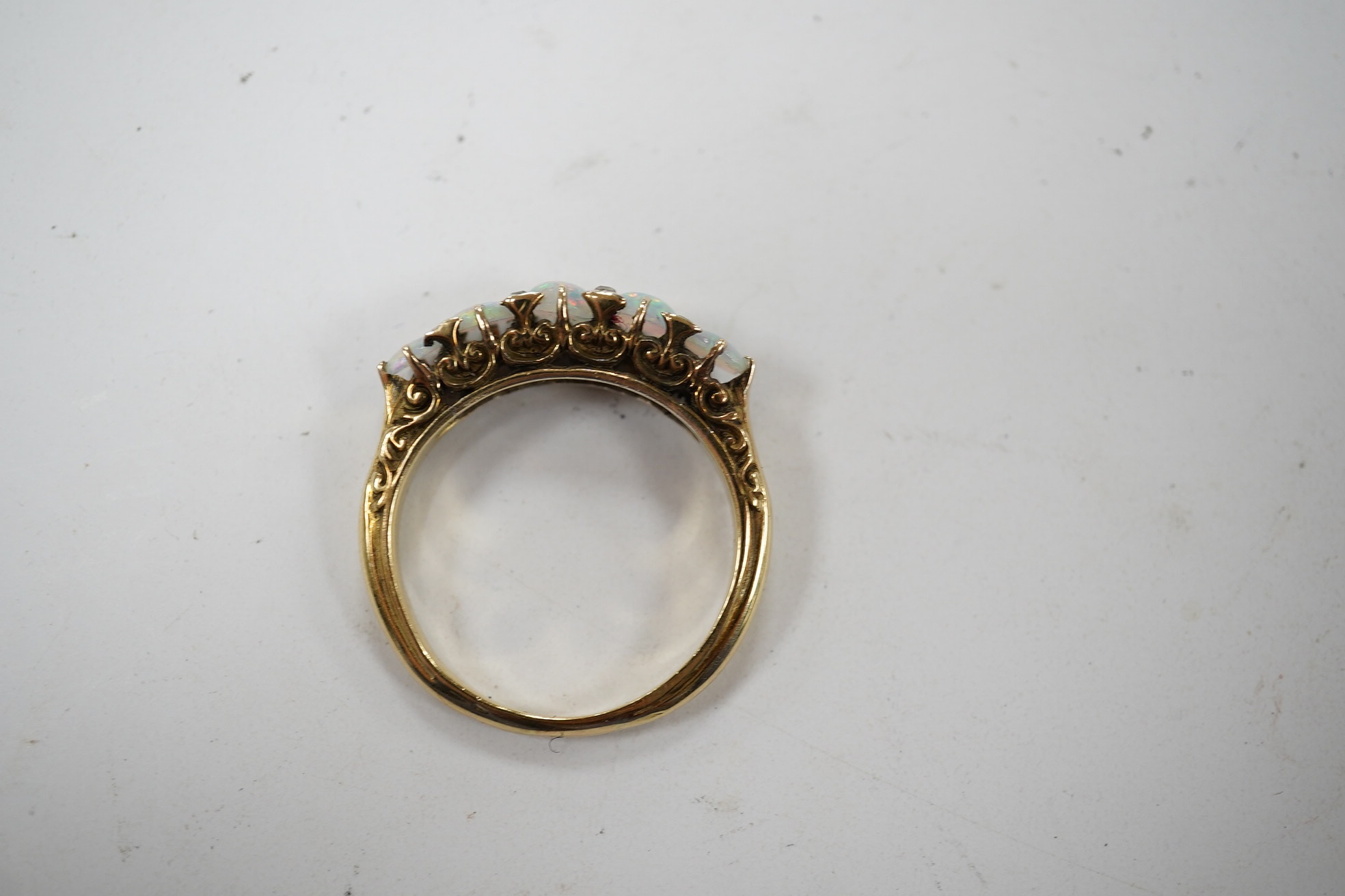 A yellow metal and graduated five stone cabochon white opal set half hoop ring, with diamond chip spacers, size Q/R, gross weight 4.6 grams. Condition - fair